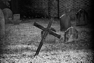 A black and white photograph of an unkempt cemetery, with a crooked grave marker.