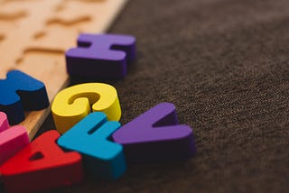 Colourful toy letters scrambled over a wooden board and a fabric patch. H, G, V, F, A, N (partially)