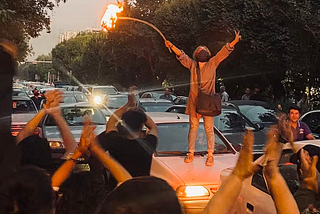 An Iranian woman protesting and holding a peace sign on top of a car.