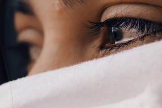 A woman’s face hidden by scarf, only teary eyes visible