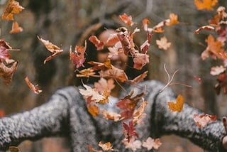 a woman with arms exttended delights in falling leaves