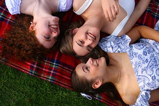 Three girls lying on a plaid blanket laughing and smiling.