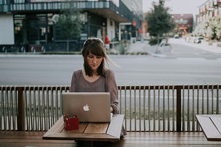 Woman sitting at a small table at a cafe outside on a gloomy day while working on her laptop