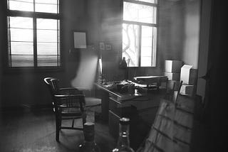 A noir-ish office in which a desk, typewriter and some bottles are visible. It could belong to a weary reporter or a cynical private eye, who knows?