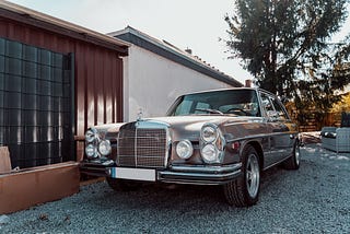 A vintage car parked in a gravel driveway in front of a house.