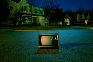 An old TV set in the middle of a neighbourhood street at night
