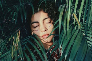 A woman laying in quiet contemplation behind palm fronds and leaves