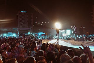 There is a spherical halo obliterating the head of a rock star on a cat walk . A crowd surrounds the protruding stage.