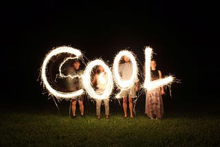 Letters COOL in bright white light with each letter held by a person