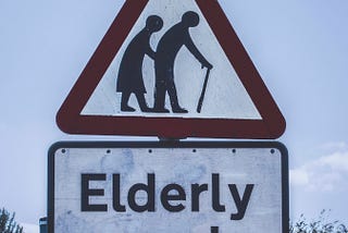 Street sign “Elderly People” with picture of an hunched over man and woman walking with a cane.