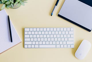 desk with keyboard, mouse, pens, notebook, and small plant