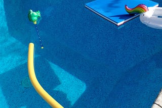 An empty pool with a yellow foam noodle and various other pool toys