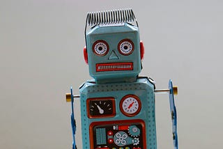 A close up photo of a blue robot toy. It has dials and clock work stickers on its metal riveted torso. The expression on its face could be interpreted to be creepy.