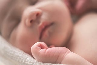 Baby, asleep. Face and chest in the background, hand in the foreground.