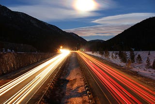 Long-exposure of car headlights over hours of traffic across a wintry nighttime highway.