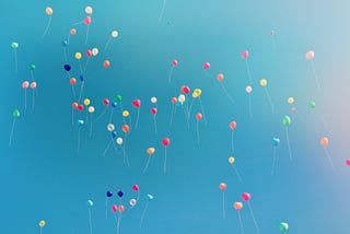 A true flock of multicolored balloons floating into a blue sky.