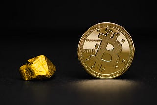 Picture of a gold nugget next to a golden coin with the bitcoin logo on it, set against a black backdop.