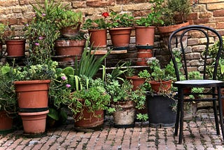 A series of several layers of terracotta pots forming a  garden, with paving and a chair.