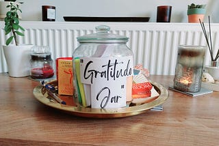 A picture of a glass jar covered with a white paper with the words “gratitude jar” amidst other deco