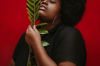 A darkskinned Black woman with a large afro holds a flower.