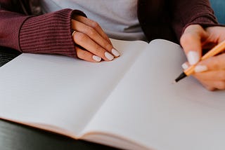 A person holds a pen to an open blank page in a journal, they are preparing to write.