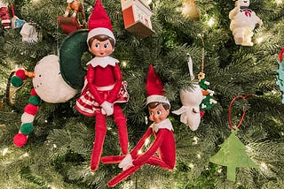 Boy and girl elf dolls sit in a Christmas tree surrounded by homemade ornaments.