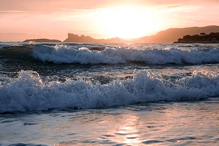 Waves crashing on sea shore. Sun rising in background.