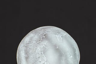 an outstretched hand set against a black background, holding a brightly lit moon