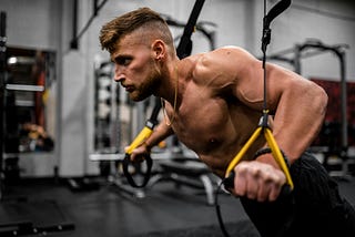 Muscular man performing push-ups on TRX bands.