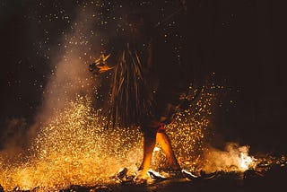 A person in shadows walking across fire-lit coals