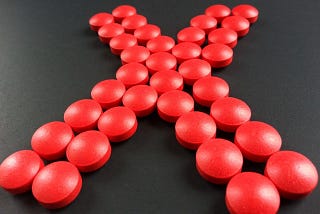 Giant “X” shape made of 32 bright red, round pills.