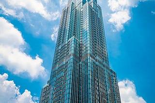 A bright skyscraper juts into puffy little clouds in a blue sky