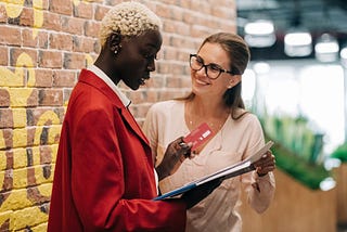 Two businesswomen in professional attire in a modern office having a positive chat about work