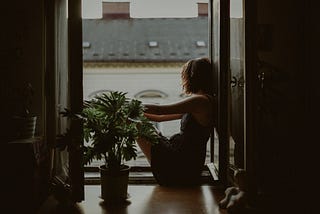 woman sat on a windowsill looking out into the street.