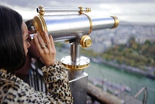 A Black woman looking through a telescope.