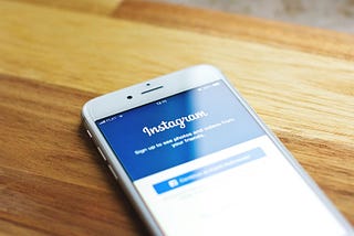 Smartphone displaying Instagram login screen with a blue background, white logo, and text encouraging users to sign up or log in.