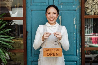 Small business owner holding a sign that the business is now open to the public, which is a form of marketing