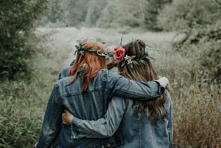 Two female friends walking with their arms around each other.