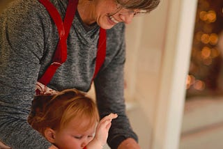 A grandma with a little girl, both wearing aprons, shaping together a ball of dough.