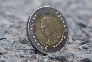 A coin with a head on it sits on a stone surface. The head is a man wearing glasses