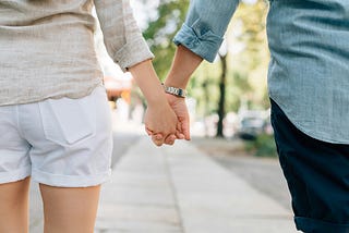 A photo of a young woman and a young man walking down the street holding hands
