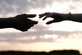Image of two people’s outstretched hands almost grasping each other indicating the persons reaching out to each other.