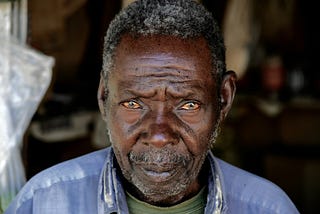 A dark man with graying hair and mournrful eyes looks at the camera.