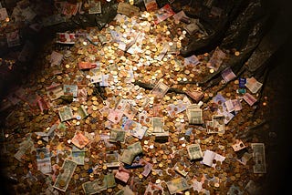 A large pile of coins and banknotes from different currencies scattered inside a container, lit from above.