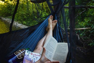 Woman in a dark blue hammock with only her feet showing because her legs are covered with books.