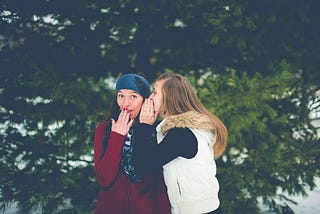 One teen girl is whispering to another teen girl.