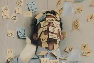 A man standing in a corner of a room. There are sticky notes covering the walls and his face.
