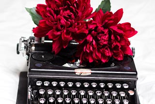 Two blooming red flowers sit on top of a black typewriter