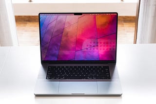 A front-facing image of an open MacBook Pro with a sunlit window behind it.