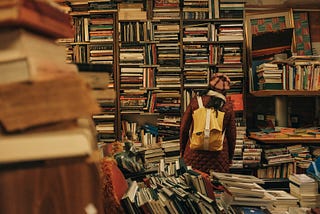 A person looking at disorganized book shelves, back toward the camera.